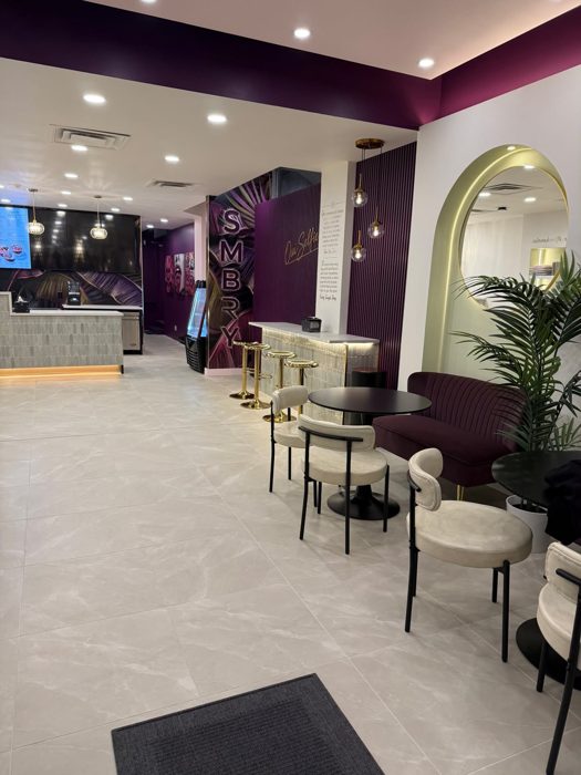 The Smashberry room seen from the entrance: ceramic counter, SMBRY wall, gold stools, plum settee and an arch with a round mirror.