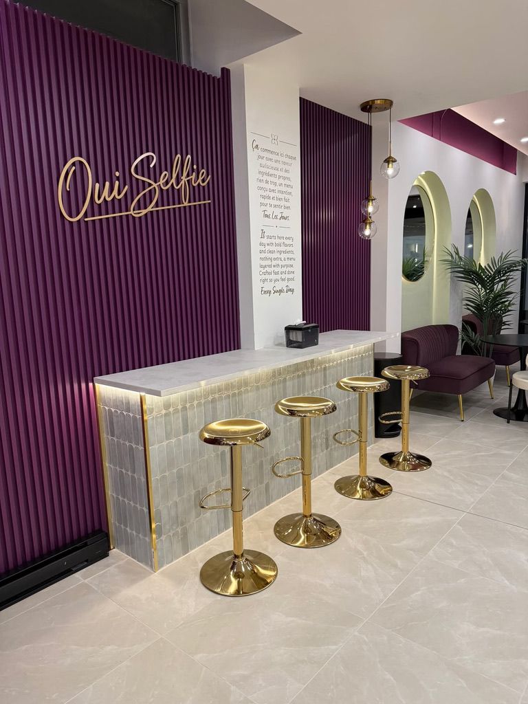 The fluted violet “Oui Selfie” wall, the ceramic counter and the gold stools.