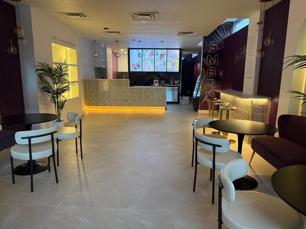 La salle de l’avenue Greene : tables noires, chaises crème, arches aux miroirs ronds et le comptoir sous les écrans du menu.