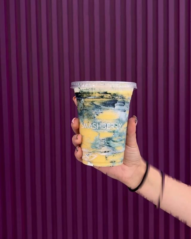 Cabana Club smoothie, mango yellow swirled with spirulina, held in front of the fluted wall.
