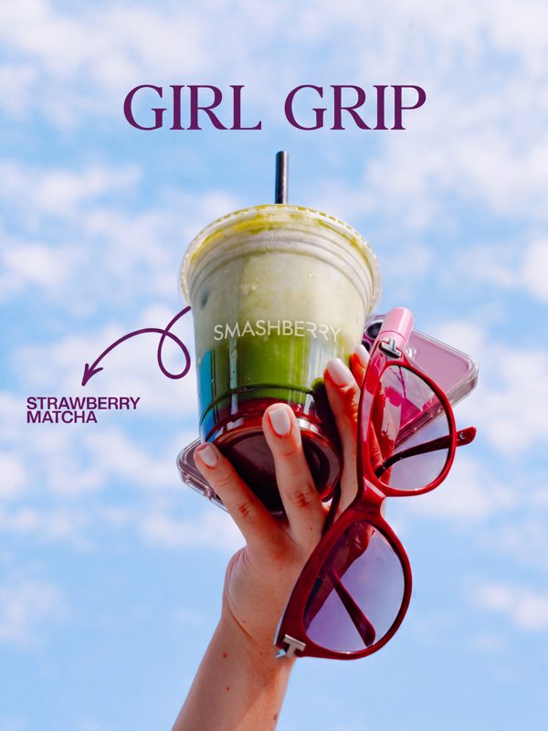 A Smashberry strawberry matcha raised against a blue sky, red sunglasses in hand.